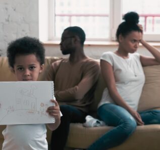 boy suffering from parents conflict at home in living room and holding picture. What Is Parallel Parenting concept