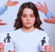 Sad young girl holding a broken piece of paper with family printed and arguing adults in the background. mandatory parenting class