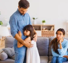 Father hugging sad young daughter while mother sits on couch. uncontested divorce if you have children