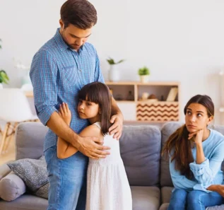 Father hugging sad young daughter while mother sits on couch. uncontested divorce if you have children